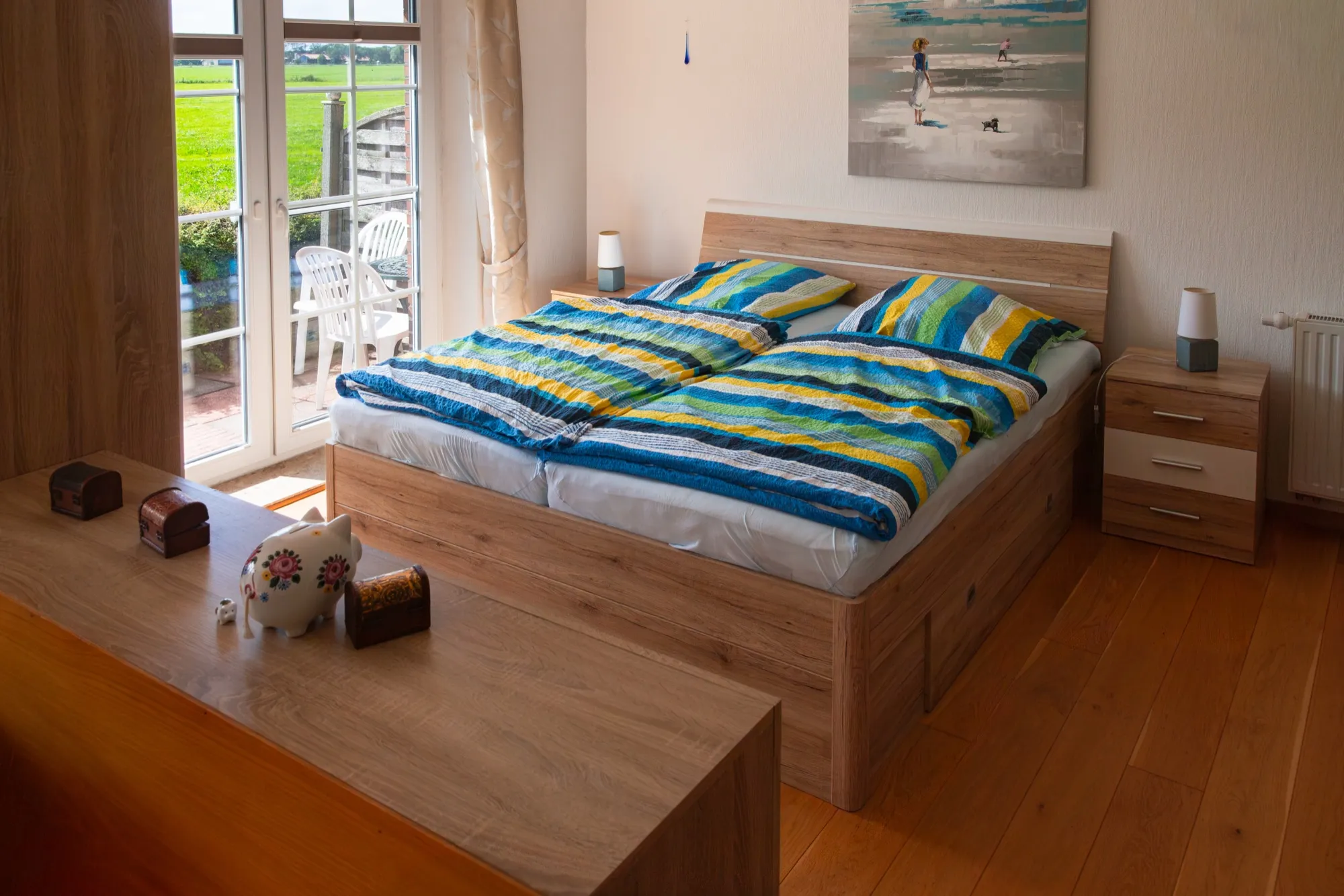 Doppelbett mit bunter Bettwäsche, Blick zum Balkon und den Feldern