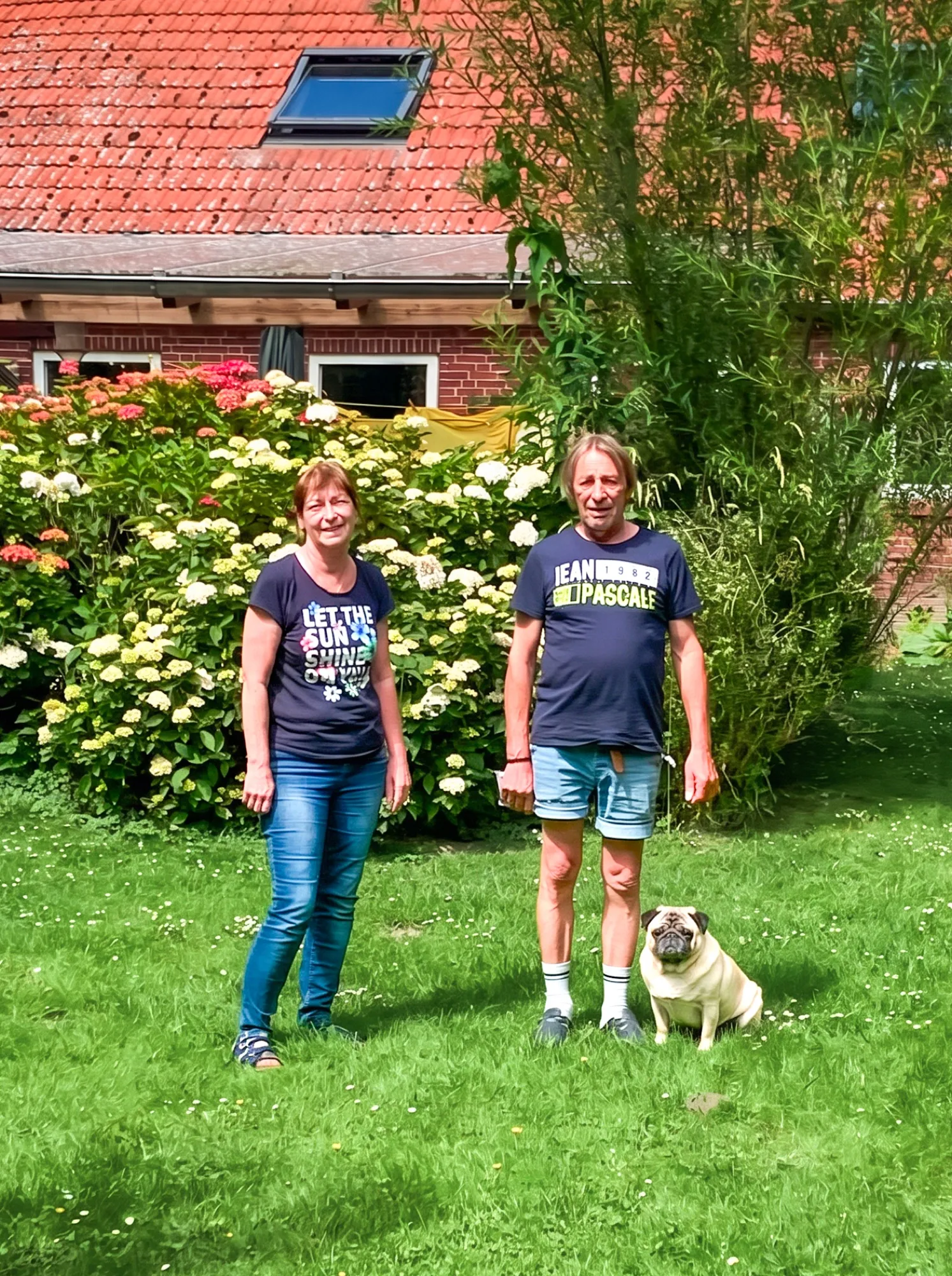 Rena und Uli stehen mit Mops Carlo im Garten vor dem Haus